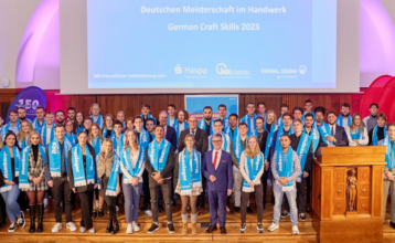 Auf dem Bild sind 81 junge Menschen mit blauen Schals zu sehen, auf denen das Logo von "Das Handwerk" ist. dazwischen stehen Senator Ties Rabe und Handwerkskammerpräsident Hjalmar Stemmann.