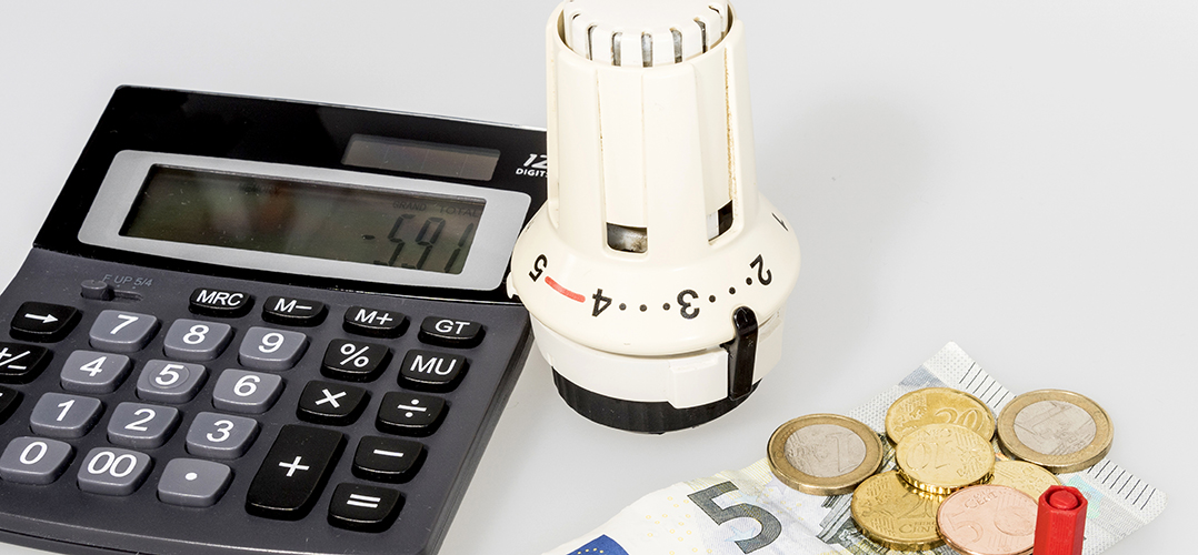 Auf dem Bild sind Euromünzen sowie eine 5 Euro-Schein, ein Taschenrechner und ein Heizungsthermostat auf weißem Bild zu sehen.