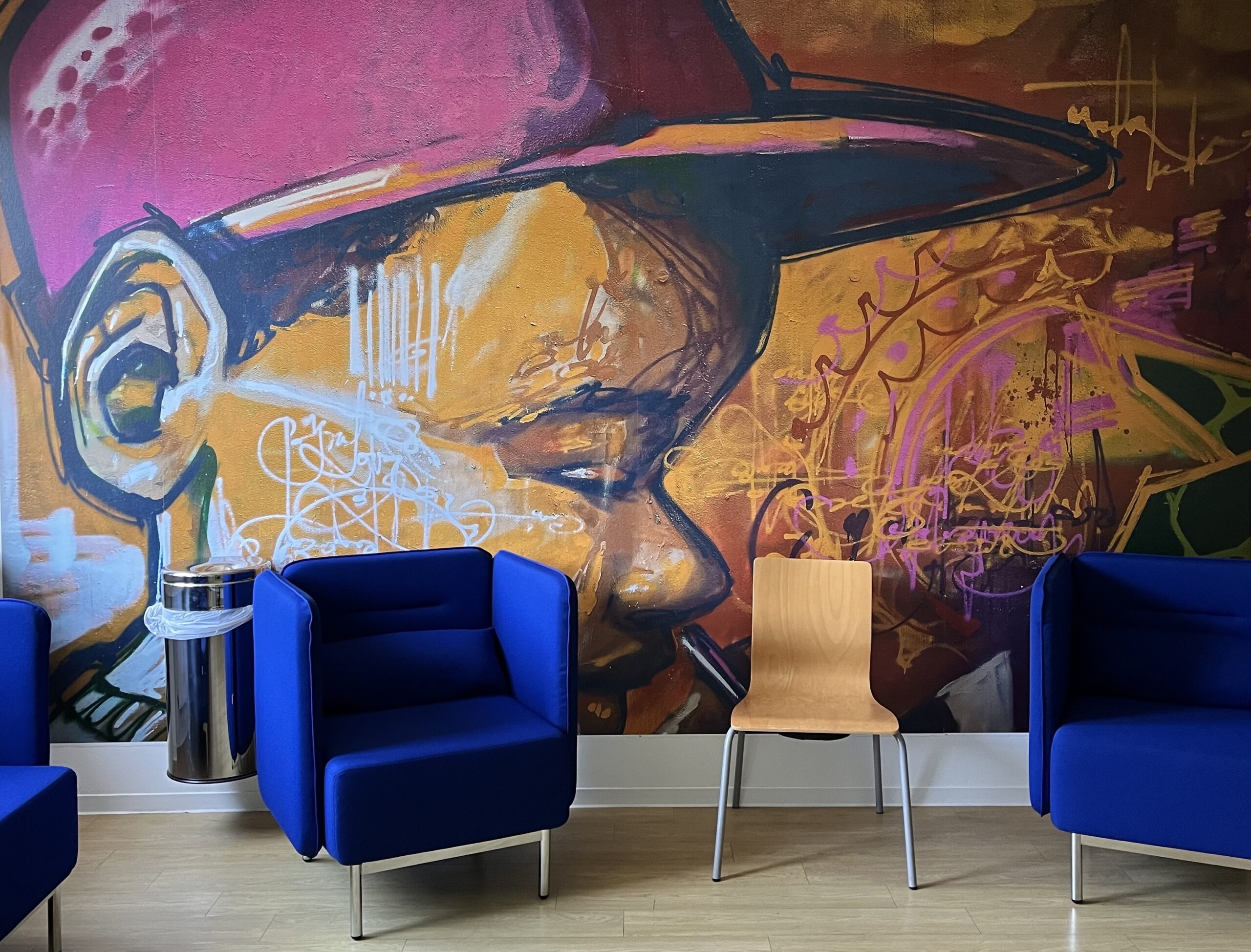 Ein Warteraum mit blauen Sesseln vor einem großen Graffiti-Wandbild.