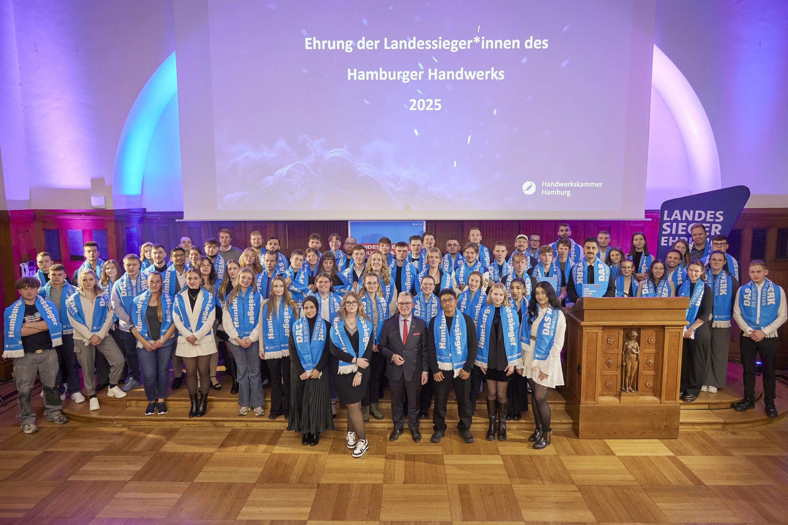Viele junge Menschen stehen auf einem Holzparkett und schauen in die Kamera.