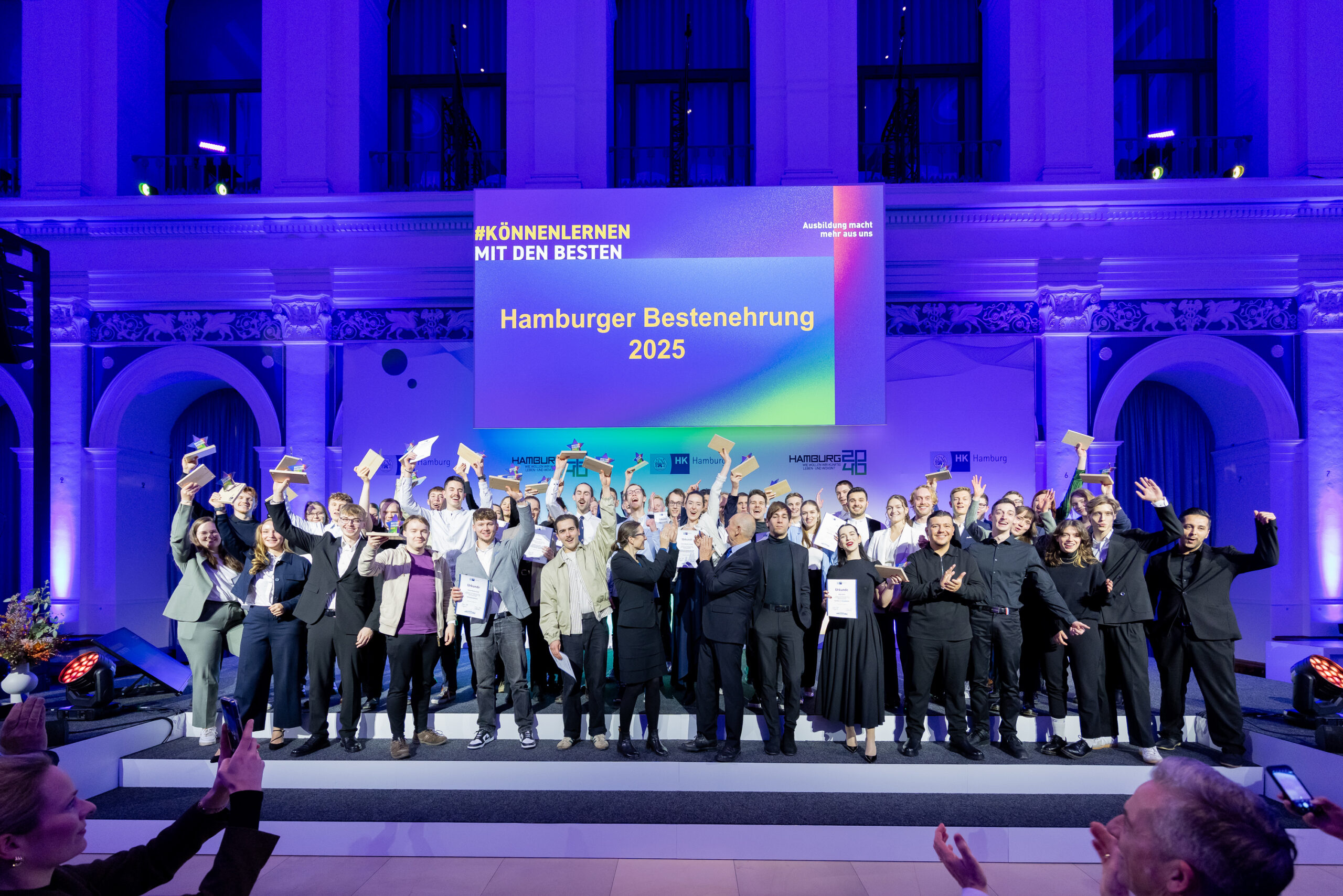 Viele junge Menschen stehen auf einer Bühne vor einem blauen Hintergrund.