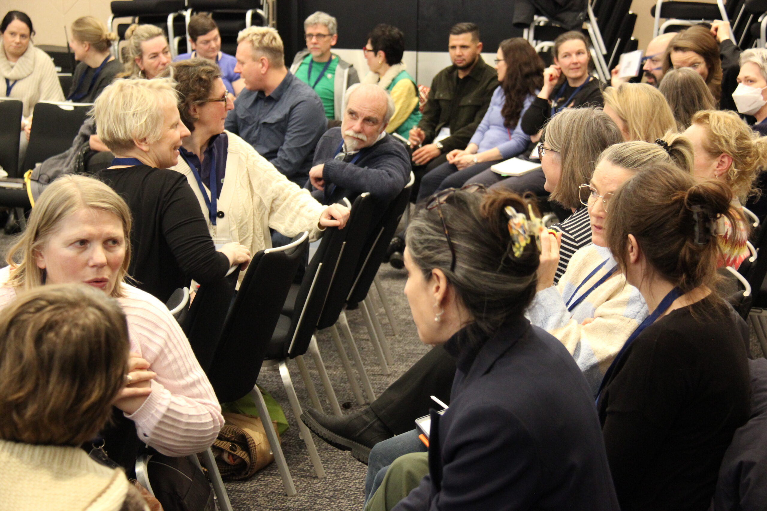 Viele Personen sitzen auf Stühlen unterhalten sich.